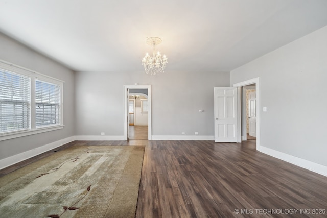 unfurnished room featuring baseboards, a notable chandelier, and dark wood-type flooring