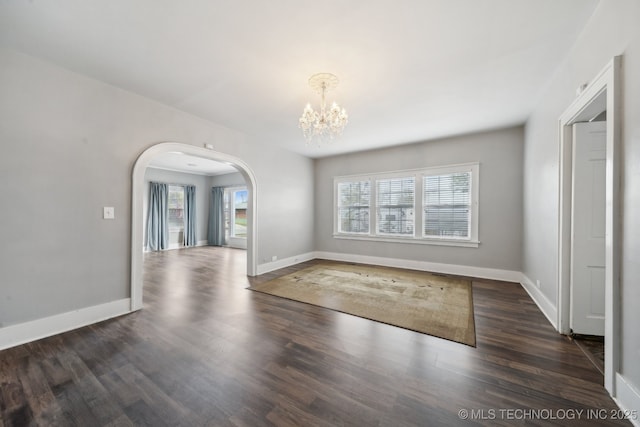 unfurnished room with a wealth of natural light, a notable chandelier, wood finished floors, and arched walkways
