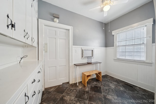 office featuring a wainscoted wall, visible vents, stone finish floor, and a ceiling fan