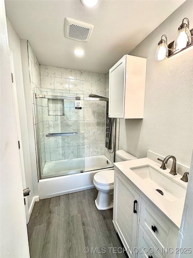 full bathroom featuring wood finished floors, toilet, vanity, visible vents, and bath / shower combo with glass door