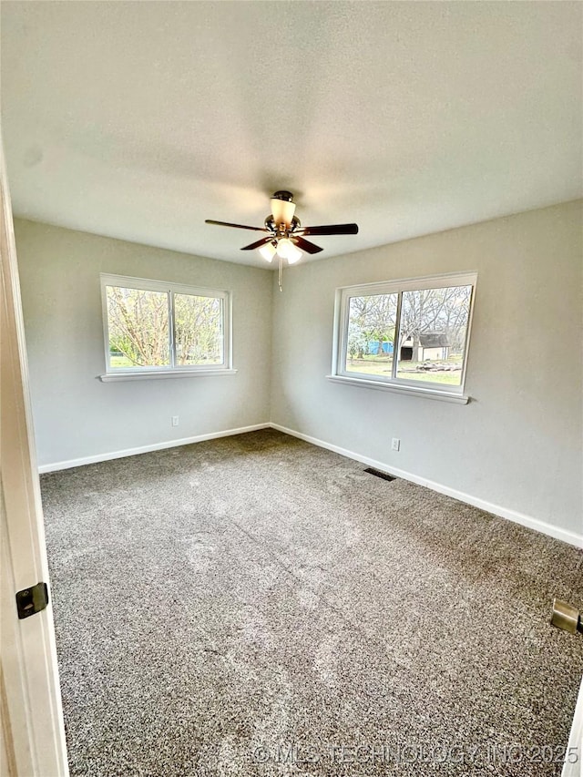 carpeted empty room with baseboards, visible vents, and ceiling fan