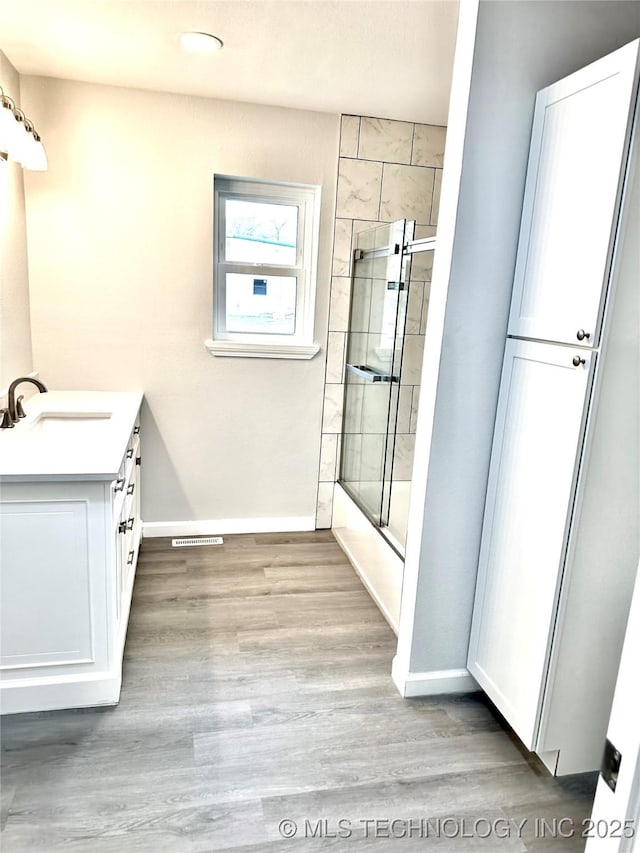 bathroom featuring bath / shower combo with glass door, visible vents, baseboards, wood finished floors, and vanity