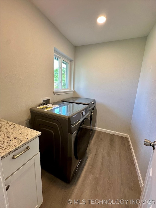 clothes washing area featuring washer and dryer, cabinet space, wood finished floors, and baseboards