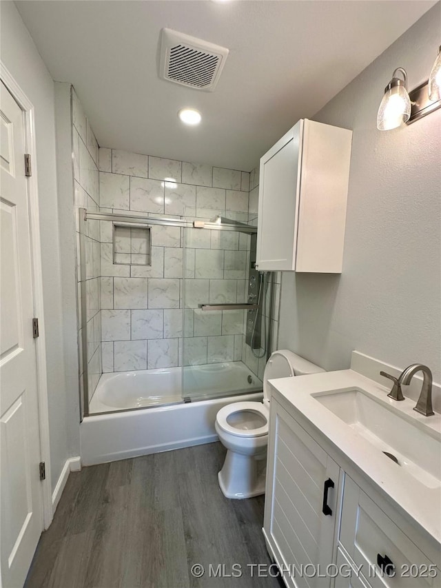 bathroom with wood finished floors, shower / bath combination with glass door, toilet, vanity, and visible vents