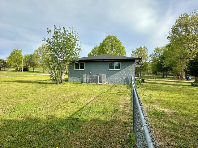 rear view of house featuring fence, a lawn, and brick siding