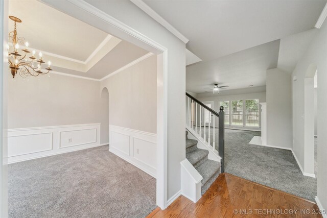 interior space with crown molding, wainscoting, arched walkways, carpet, and ceiling fan with notable chandelier