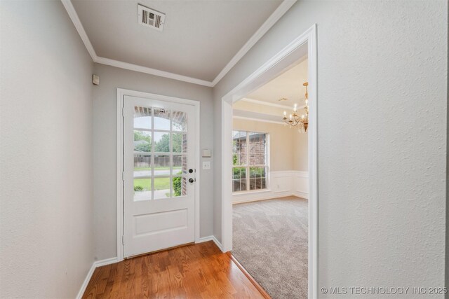 entryway featuring visible vents, crown molding, wood finished floors, and a notable chandelier