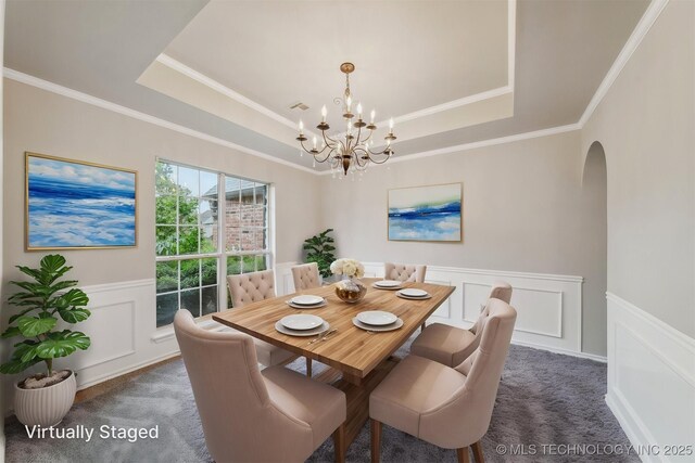 dining space with an inviting chandelier, arched walkways, dark carpet, a wainscoted wall, and a tray ceiling