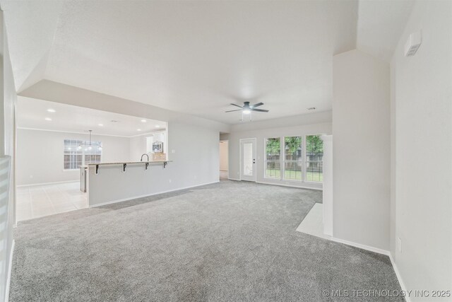 unfurnished living room featuring a healthy amount of sunlight, baseboards, light carpet, and ceiling fan with notable chandelier
