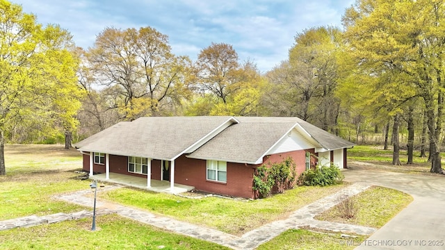 view of front of property featuring brick siding, driveway, a front lawn, and covered porch