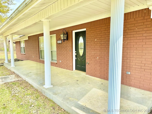 doorway to property with covered porch and brick siding