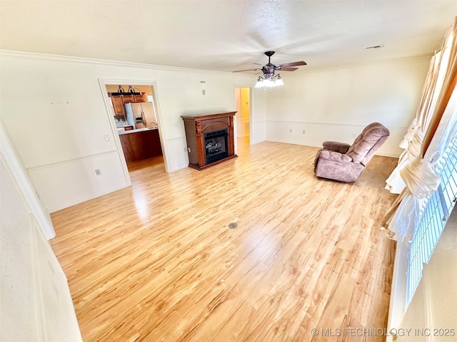 unfurnished living room with crown molding, a fireplace, a ceiling fan, visible vents, and wood finished floors