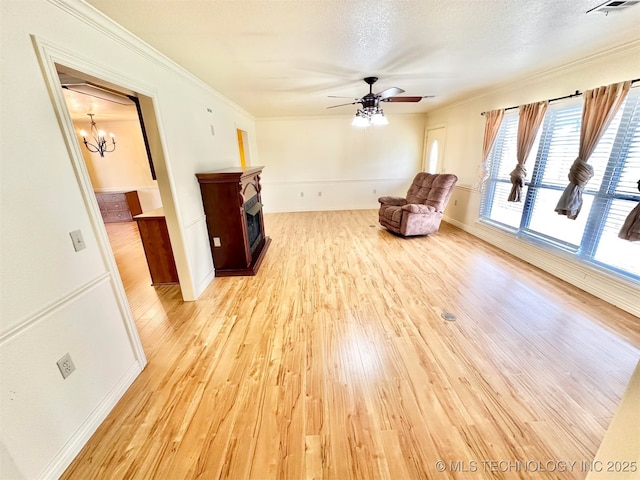 unfurnished room featuring ceiling fan with notable chandelier, a fireplace, light wood-type flooring, ornamental molding, and baseboards