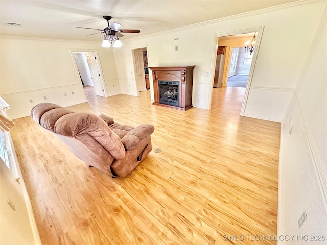 living room with visible vents, a fireplace, crown molding, light wood finished floors, and ceiling fan with notable chandelier