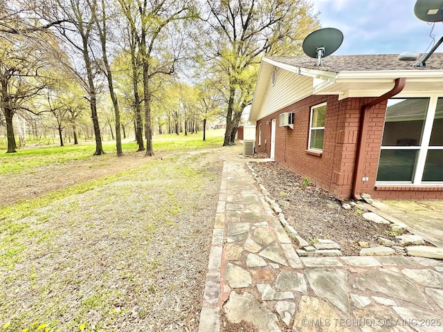 view of side of home with central air condition unit, a wall mounted AC, a lawn, and brick siding