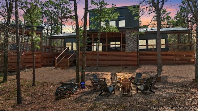 1739 NW 136th Rd, Wilburton, OK 74578 - back of house at dusk featuring an outdoor fire pit, a sunroom, stairway, and metal roof