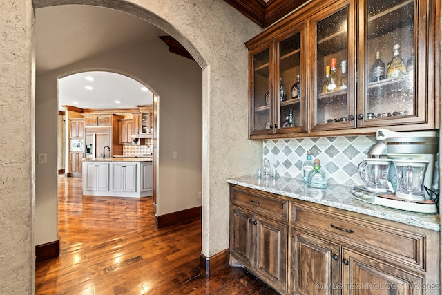 9931 N Chadford Rd, Owasso, OK 74055 - bar with arched walkways, dark wood-style flooring, paneled built in refrigerator, decorative backsplash, and a textured wall