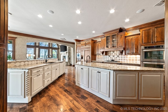 9931 N Chadford Rd, Owasso, OK 74055 - kitchen featuring double oven, a large island with sink, cooktop, ornamental molding, and arched walkways
