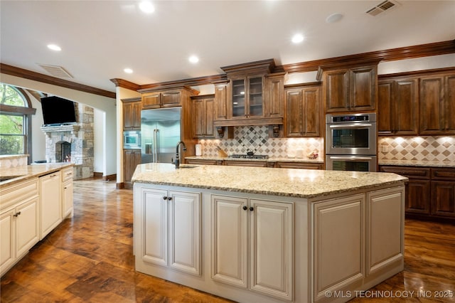 kitchen with visible vents, crown molding, a center island with sink, a sink, and built in appliances