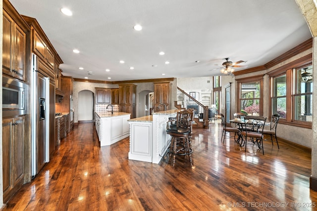 9931 N Chadford Rd, Owasso, OK 74055 - kitchen featuring arched walkways, a center island with sink, built in appliances, crown molding, and ceiling fan
