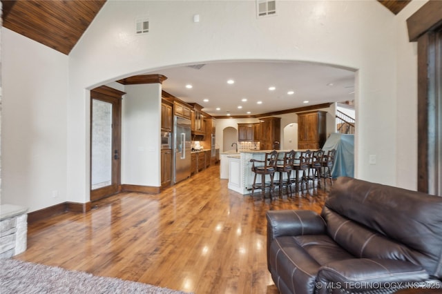 living room with arched walkways, visible vents, ornate columns, and light wood-style floors