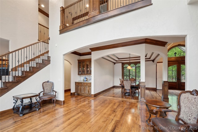 interior space featuring arched walkways, wood finished floors, ornamental molding, a high ceiling, and stairs