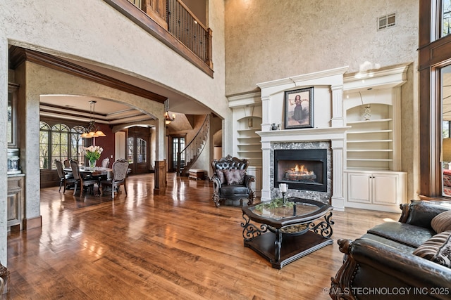 9931 N Chadford Rd, Owasso, OK 74055 - living room with arched walkways, a high ceiling, a warm lit fireplace, built in shelves, and stairs