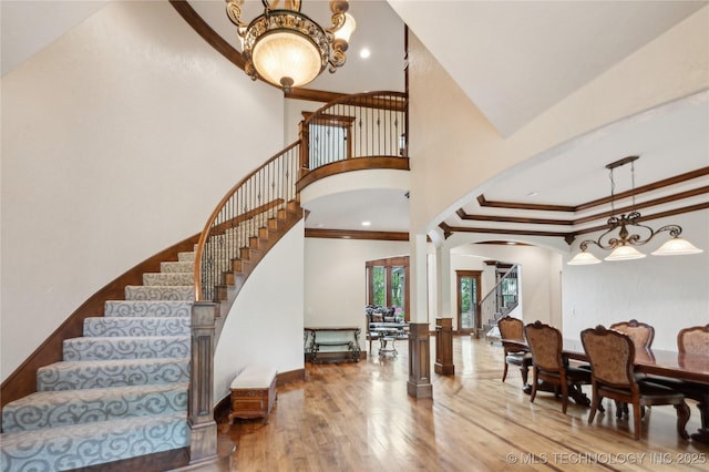 entrance foyer with crown molding, wood finished floors, a high ceiling, stairway, and arched walkways