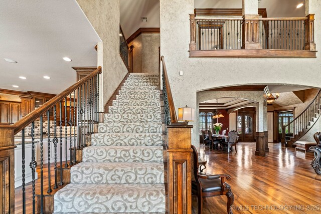 9931 N Chadford Rd, Owasso, OK 74055 - staircase featuring arched walkways, wood finished floors, a towering ceiling, crown molding, and a textured wall