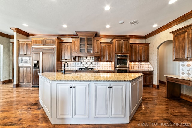 9931 N Chadford Rd, Owasso, OK 74055 - kitchen featuring built in appliances, a large island with sink, crown molding, arched walkways, and dark wood-style floors