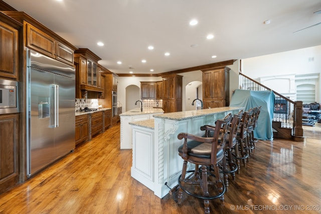 9931 N Chadford Rd, Owasso, OK 74055 - kitchen featuring arched walkways, built in appliances, a center island with sink, backsplash, and wood finished floors