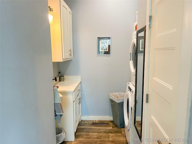 laundry area featuring stacked washer and clothes dryer, cabinet space, dark wood-style floors, and baseboards