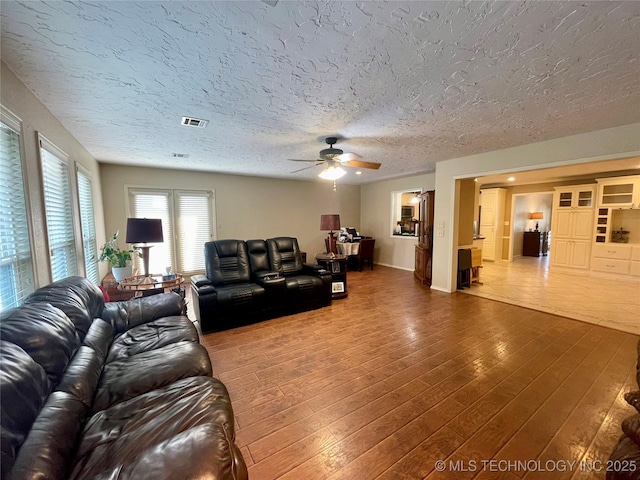 living area featuring a textured ceiling, visible vents, hardwood / wood-style flooring, and a ceiling fan