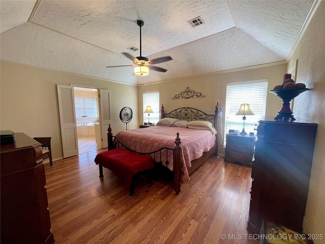 bedroom with vaulted ceiling, wood finished floors, a textured ceiling, visible vents, and ornamental molding