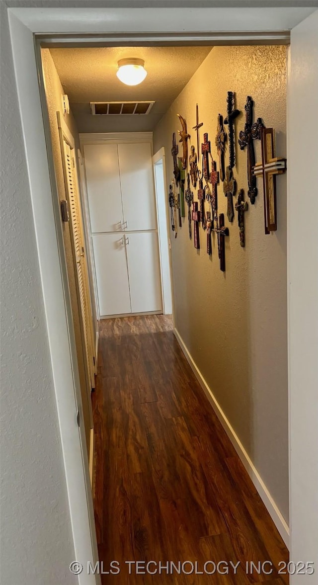 hallway featuring dark wood-type flooring, baseboards, a textured ceiling, and visible vents