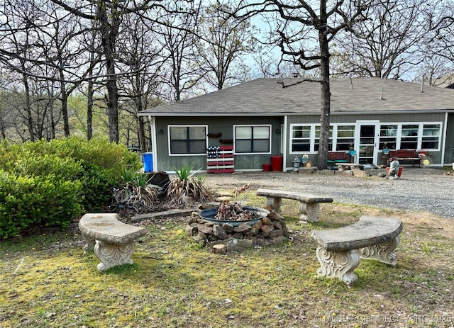 rear view of property with a shingled roof and an outdoor fire pit