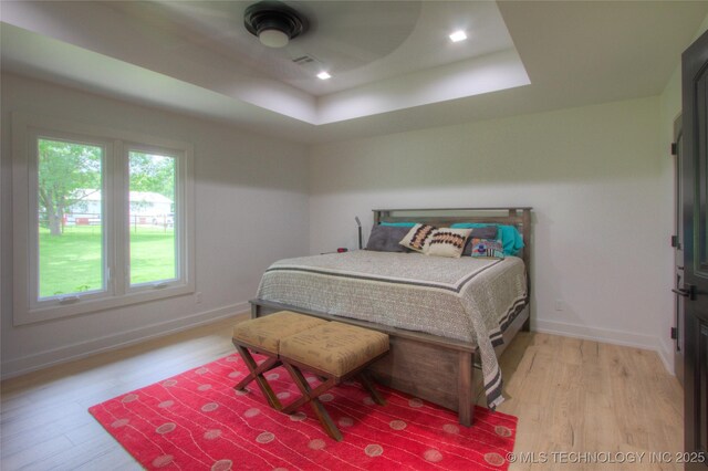 bedroom featuring baseboards, a raised ceiling, light wood-style floors, and visible vents