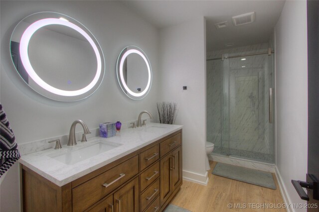bathroom with a sink, toilet, wood finished floors, a marble finish shower, and double vanity