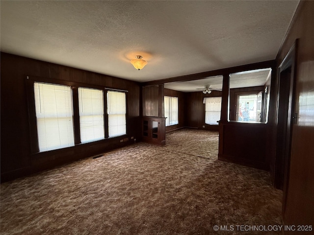 609 N E St, Mcalester, OK 74501 - unfurnished living room featuring a textured ceiling, wood walls, ceiling fan, and carpet