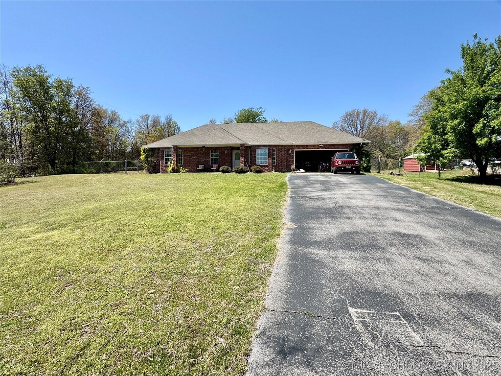 ranch-style house featuring an attached garage, fence, brick siding, a front lawn, and driveway