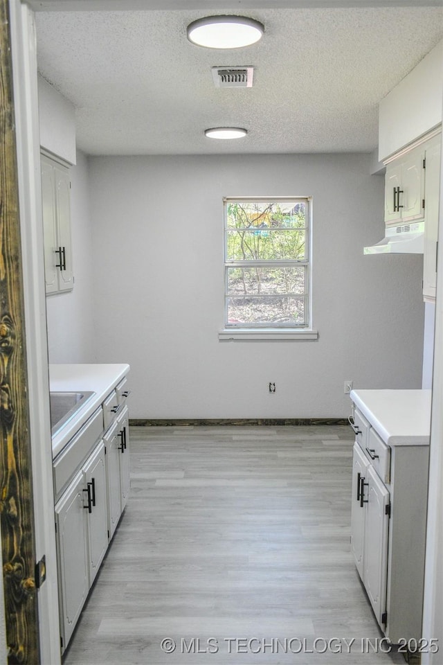 kitchen featuring visible vents, light countertops, under cabinet range hood, and light wood-type flooring