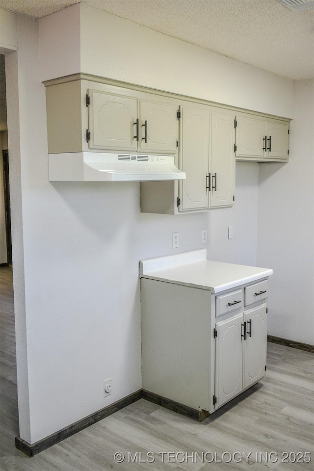 kitchen with light countertops, a textured ceiling, light wood-type flooring, under cabinet range hood, and baseboards