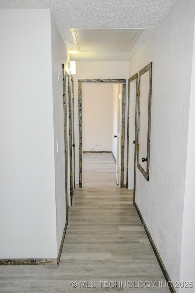 corridor with light wood-style flooring and a textured ceiling
