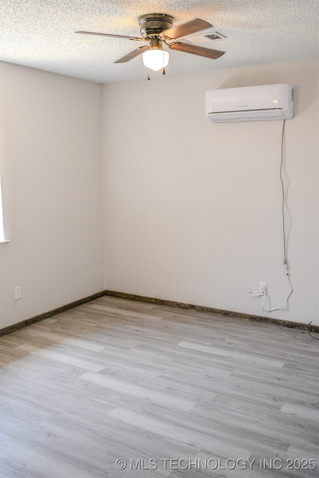 unfurnished room with a wall unit AC, wood finished floors, ceiling fan, and a textured ceiling