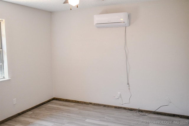 spare room featuring a ceiling fan, a textured ceiling, light wood-style flooring, a wall mounted air conditioner, and baseboards