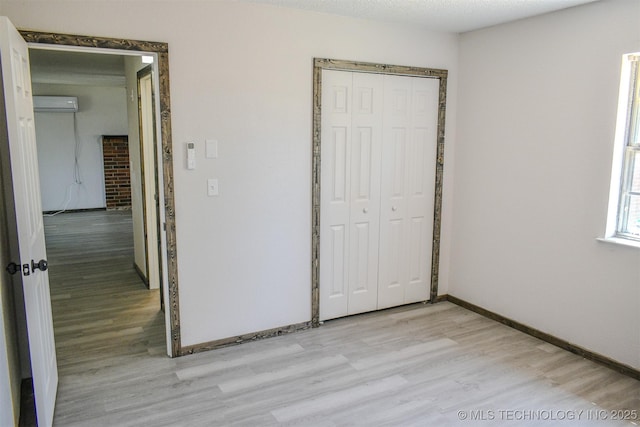unfurnished bedroom with baseboards, a closet, light wood-style floors, and an AC wall unit
