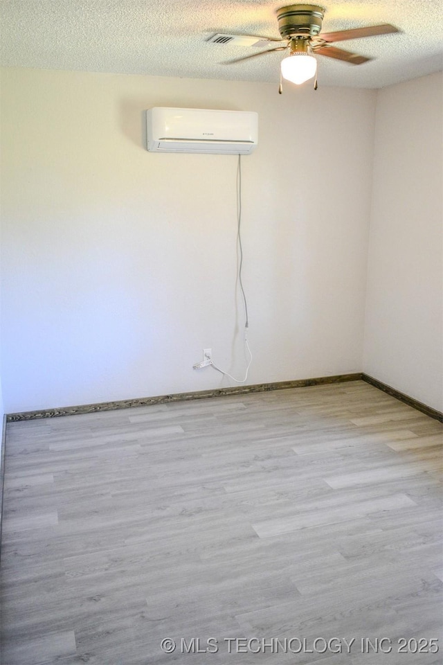 empty room with a textured ceiling, wood finished floors, an AC wall unit, and a ceiling fan