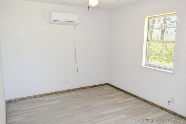 unfurnished room featuring a wall mounted AC, baseboards, ceiling fan, and light wood-type flooring