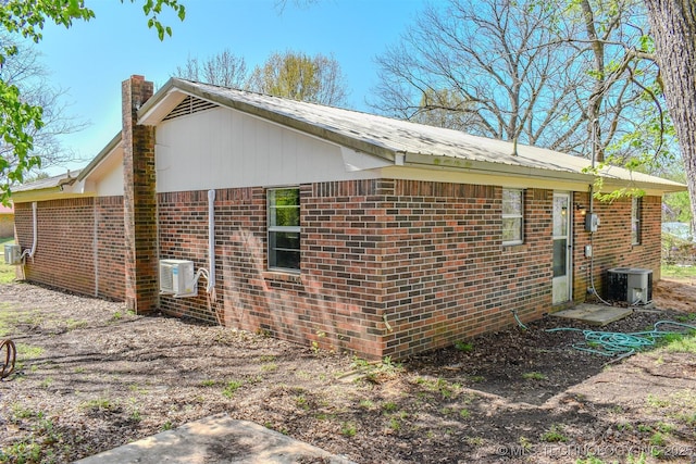 view of side of property featuring central air condition unit, a chimney, and brick siding