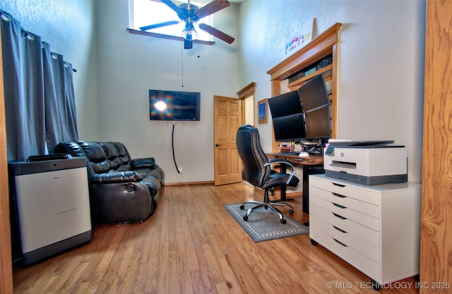 office area featuring a high ceiling, light wood-style flooring, and ceiling fan